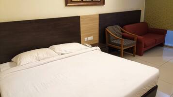 Een hotelkamer met een groot bed, een houten hoofdeinde, een rode bank en een aan de muur bevestigd fotolijstje.