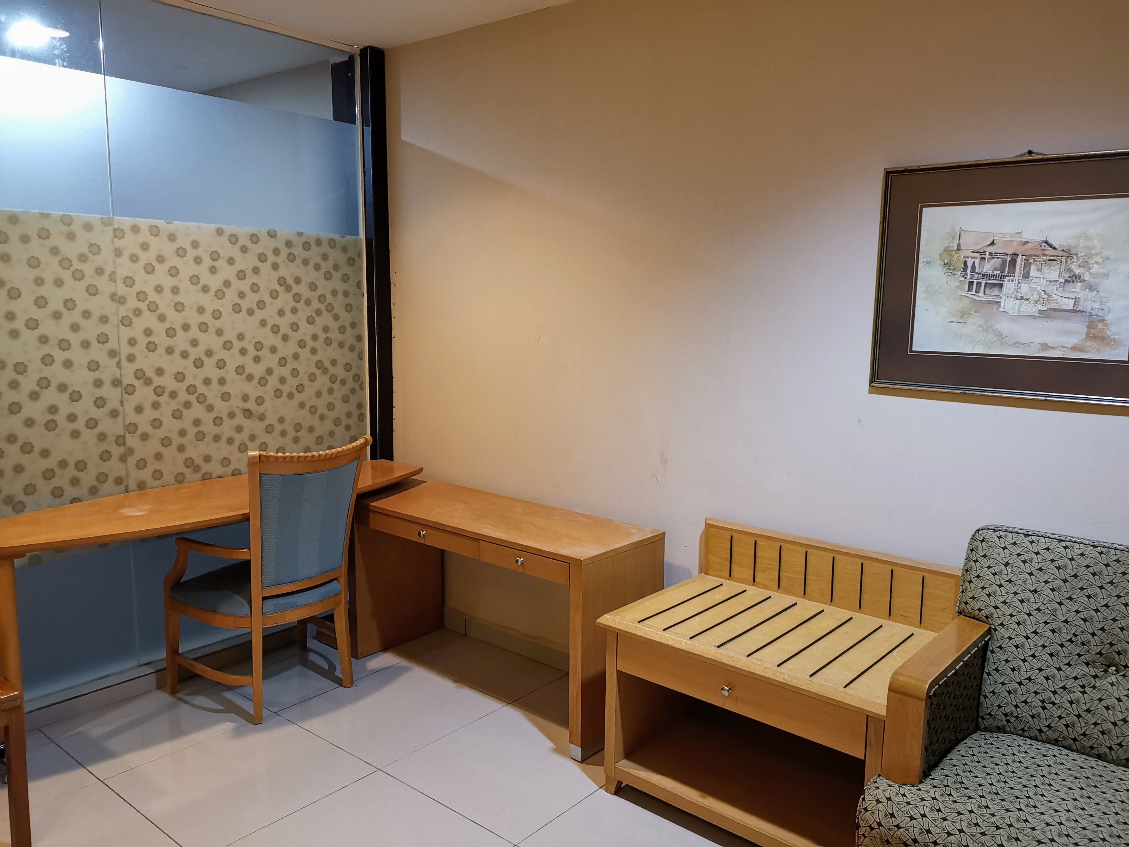 Une pièce comprenant un bureau en bois, une chaise, une petite table en bois et un canapé à motifs.