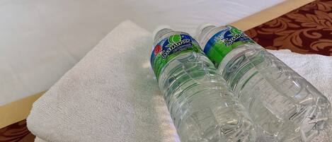 Two clear plastic bottles of water on a white towel on a bed.