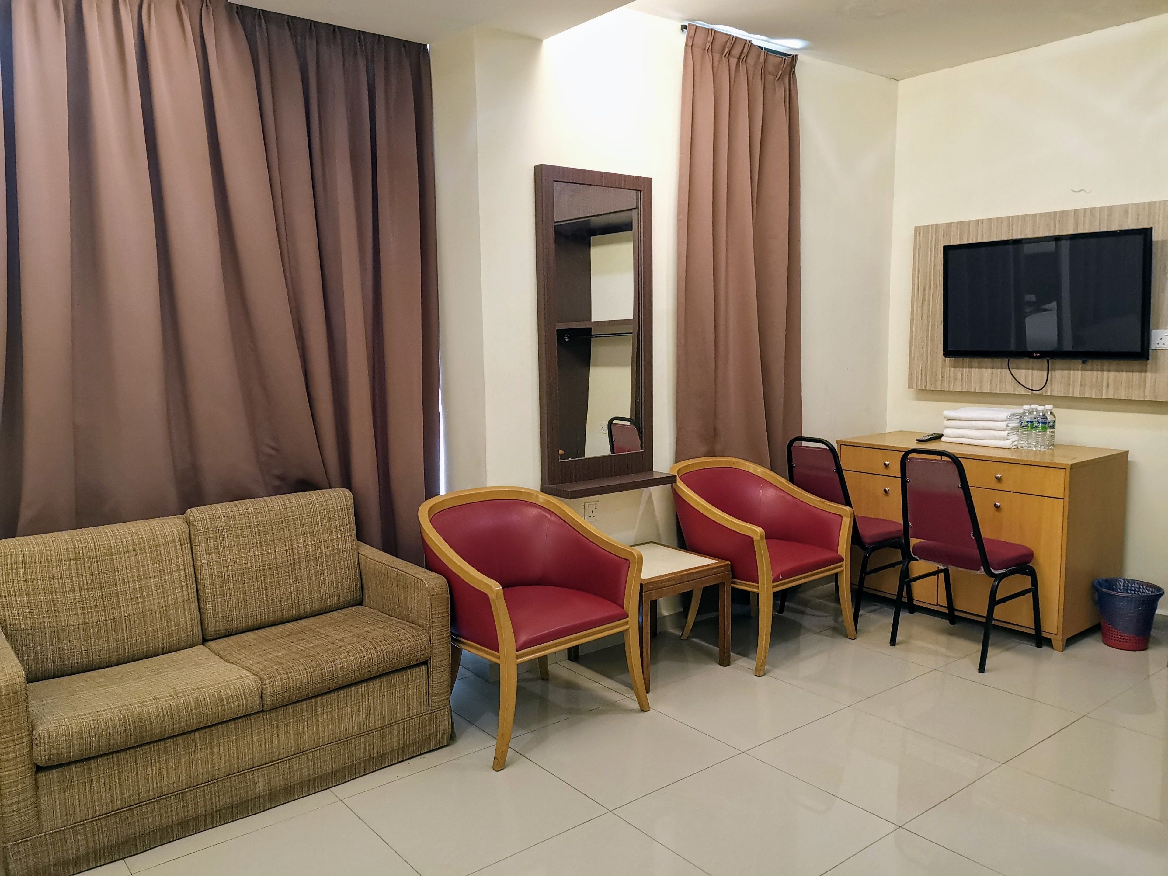 Ein Hotelzimmer mit einer Couch, zwei roten Sesseln, einem Holztisch mit Fernseher und einem Spiegel an der Wand.