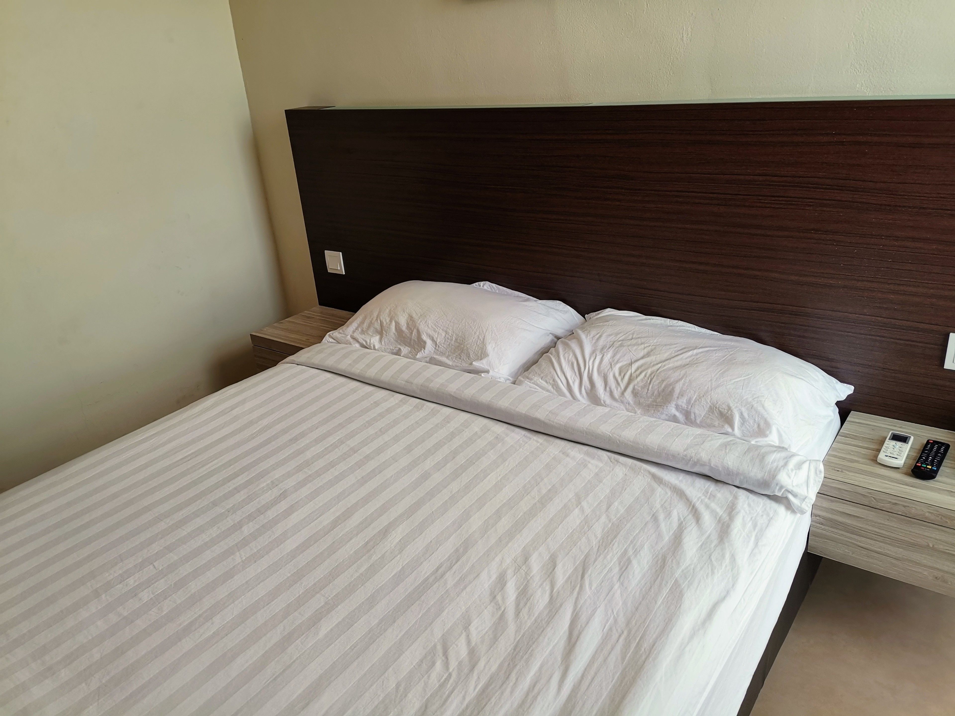 A neatly made bed with white linens, a wooden headboard, and a bedside table with a remote control.