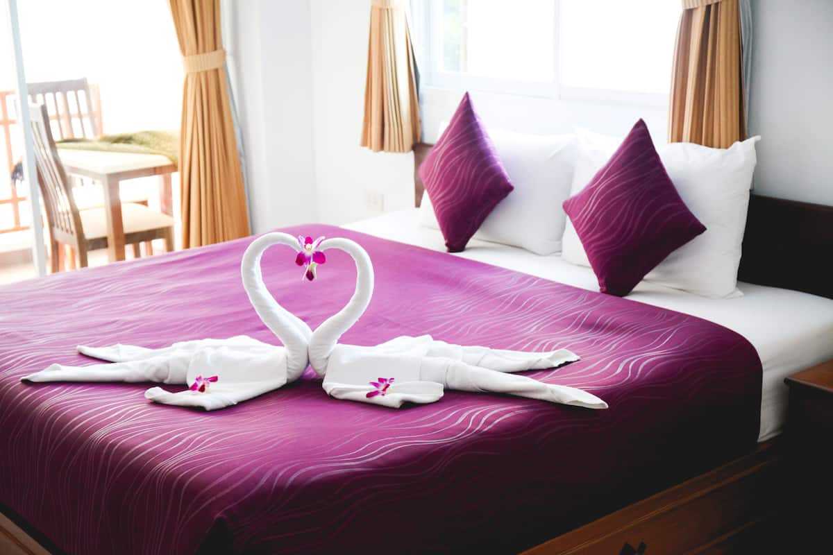 Quarto de hotel com cama, roupa de cama roxa, almofadas brancas e arranjo de toalha em formato de cisne.