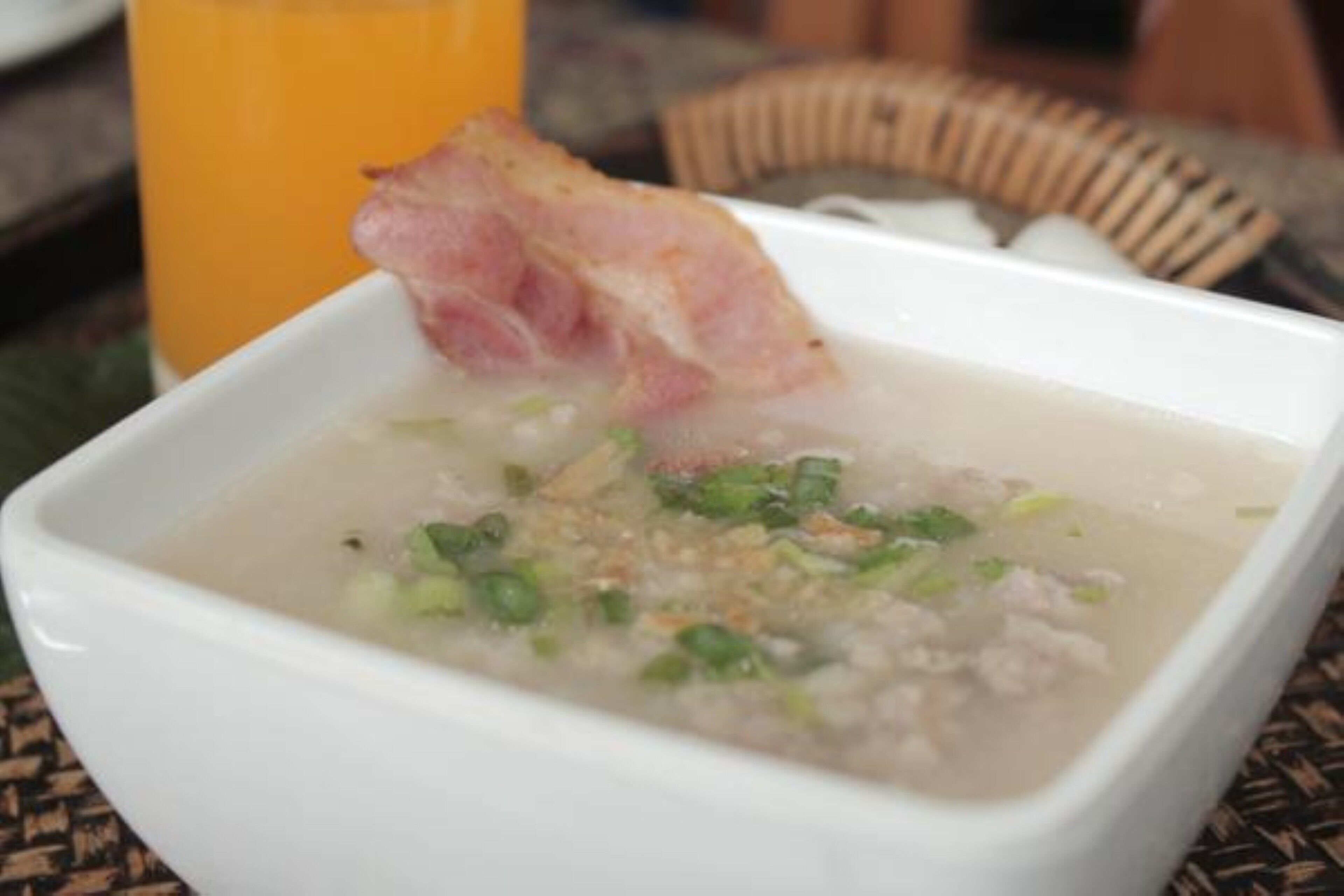A bowl of soup with meat and green onions, accompanied by a glass of orange juice.
