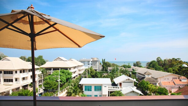 Ein Balkon mit einem großen Sonnenschirm, mit Blick auf eine Wohngegend mit verschiedenen Gebäuden und freiem Blick auf das Meer.