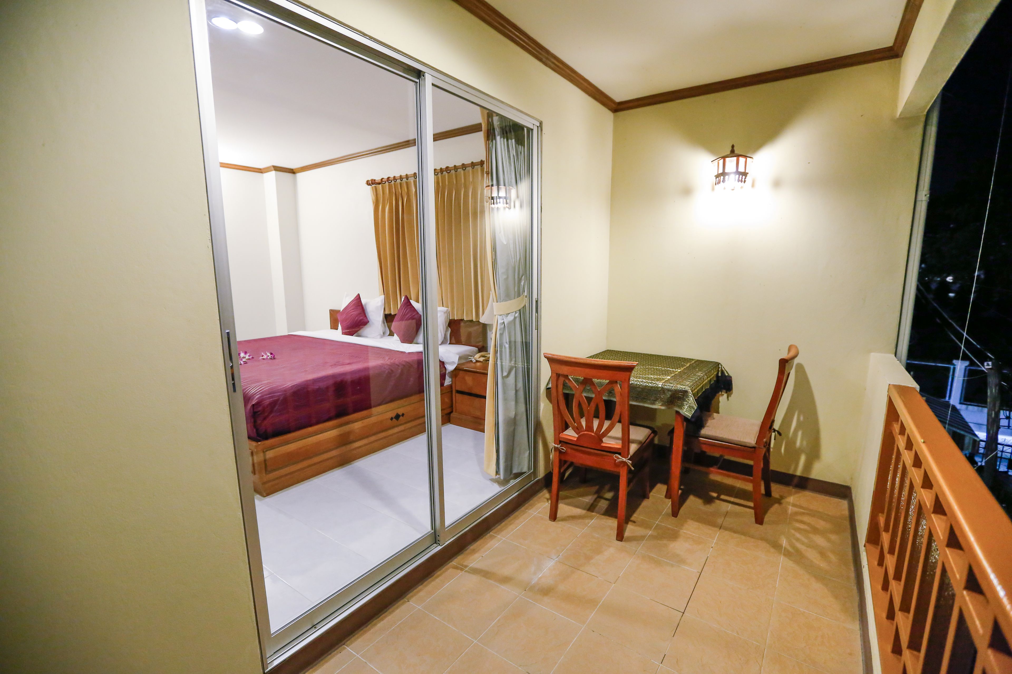 Un dormitorio con puerta corredera, cama, mesita de noche, silla, mesa y balcón con barandilla.