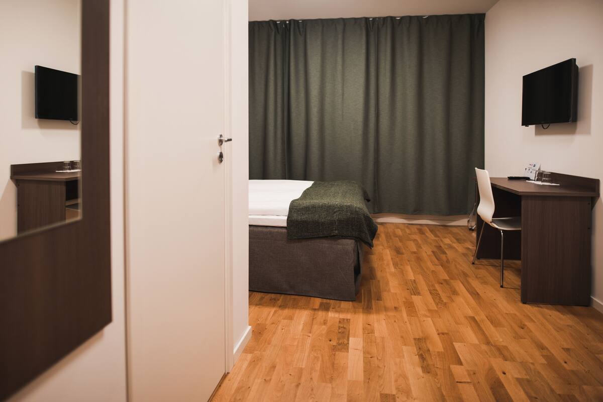 Ett hotellrum med en säng, ett skrivbord, en stol, en tv och en spegel.