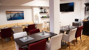 Zona pranzo moderna con diversi tavoli e sedie, una TV a schermo piatto montata a parete e pavimento in legno.