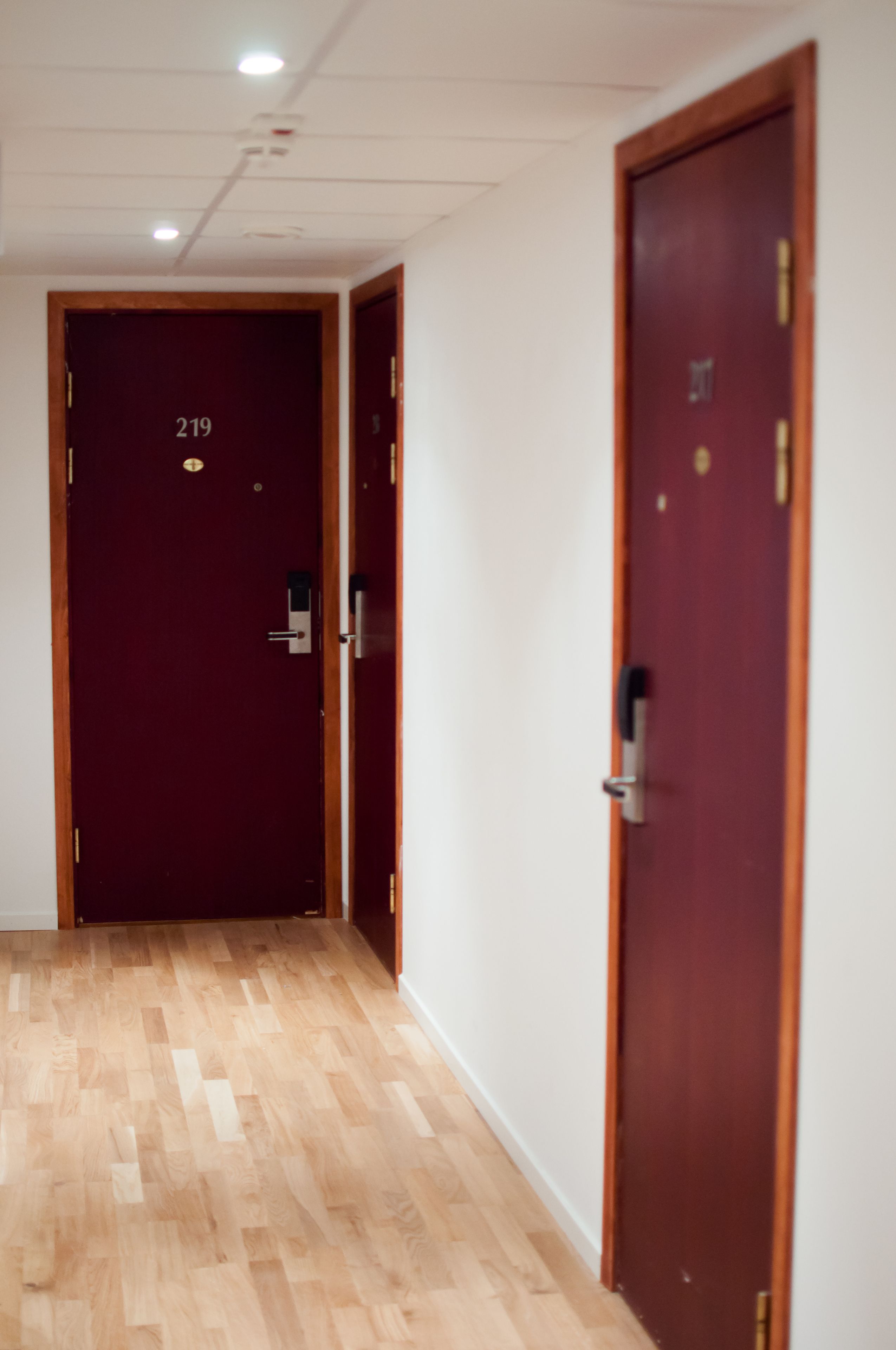 A hallway with wooden flooring and two closed doors, one marked with the number 219.