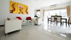 Una sala de estar moderna con un sofá blanco, una mesa de centro de vidrio y un área de comedor con una mesa y sillas.