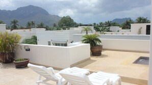Terraza en la azotea con sillas de plástico blanco y plantas en macetas, con vistas a un paisaje montañoso.