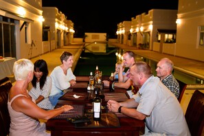 A group of people dining at an outdoor table with a pool in the background. - Talay Tara Resort (Sam Roi Yot)