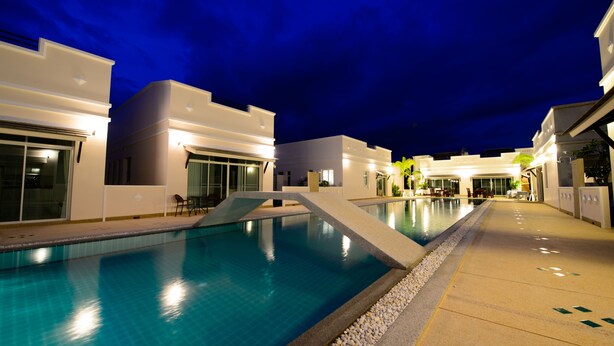 Una piscina con superficie de agua azul cristalina, rodeada de edificios modernos con grandes ventanales e iluminación exterior.