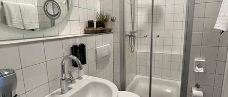 A modern bathroom with a white sink, toilet, and glass-enclosed shower.