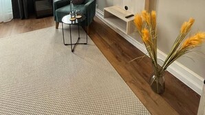 Un salon moderne avec un fauteuil turquoise, un téléviseur à écran plat fixé au mur, une petite table d’appoint avec un verre et un vase contenant des plantes séchées.