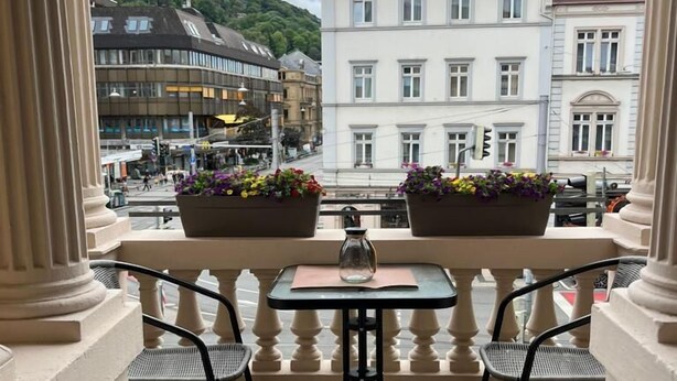 Un balcon avec une table et des chaises, donnant sur un paysage urbain avec des immeubles et une colline.