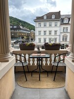 Un balcón con dos sillas y una mesa, con vistas a una calle con edificios y una colina.