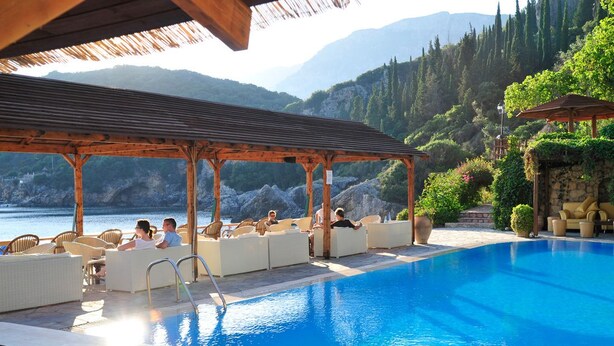 Zona de piscina con sillas de descanso y una pérgola con vistas a un cuerpo de agua y montañas.