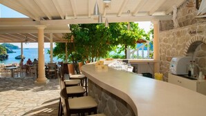 Zona de bar al aire libre con columnas de piedra, una barra curva y lámparas colgantes.