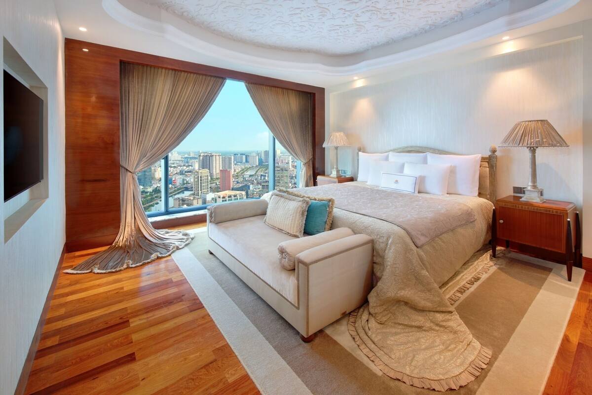 Habitación de hotel moderna con una cama grande, un sofá, un televisor y vistas a la ciudad.