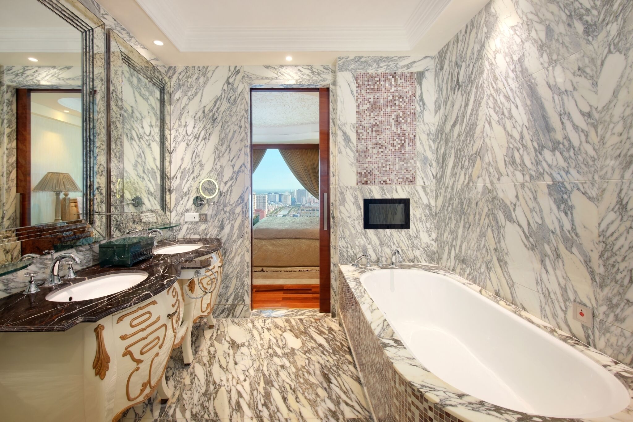 Une salle de bain luxueuse avec des murs en marbre, une grande baignoire et une vue sur la ville, visible à travers une porte.