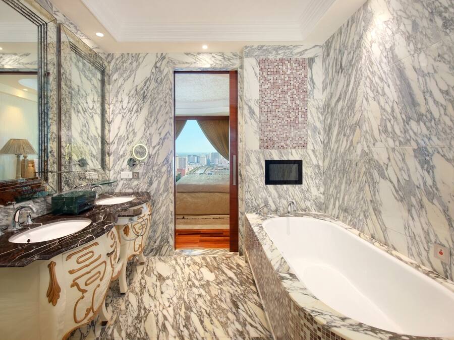 Une salle de bain luxueuse avec des murs en marbre, une grande baignoire et une vue sur la ville, visible à travers une porte.