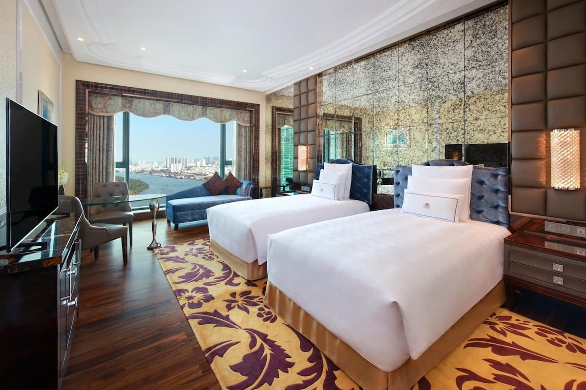 Habitación de hotel con dos camas, televisión, escritorio y vista a la ciudad.