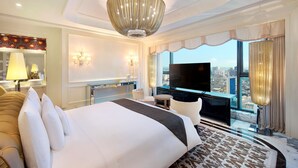 Ein Hotelzimmer mit einem großen Bett, einem Fernseher, einer Chandelüster und Blick auf die Stadt.