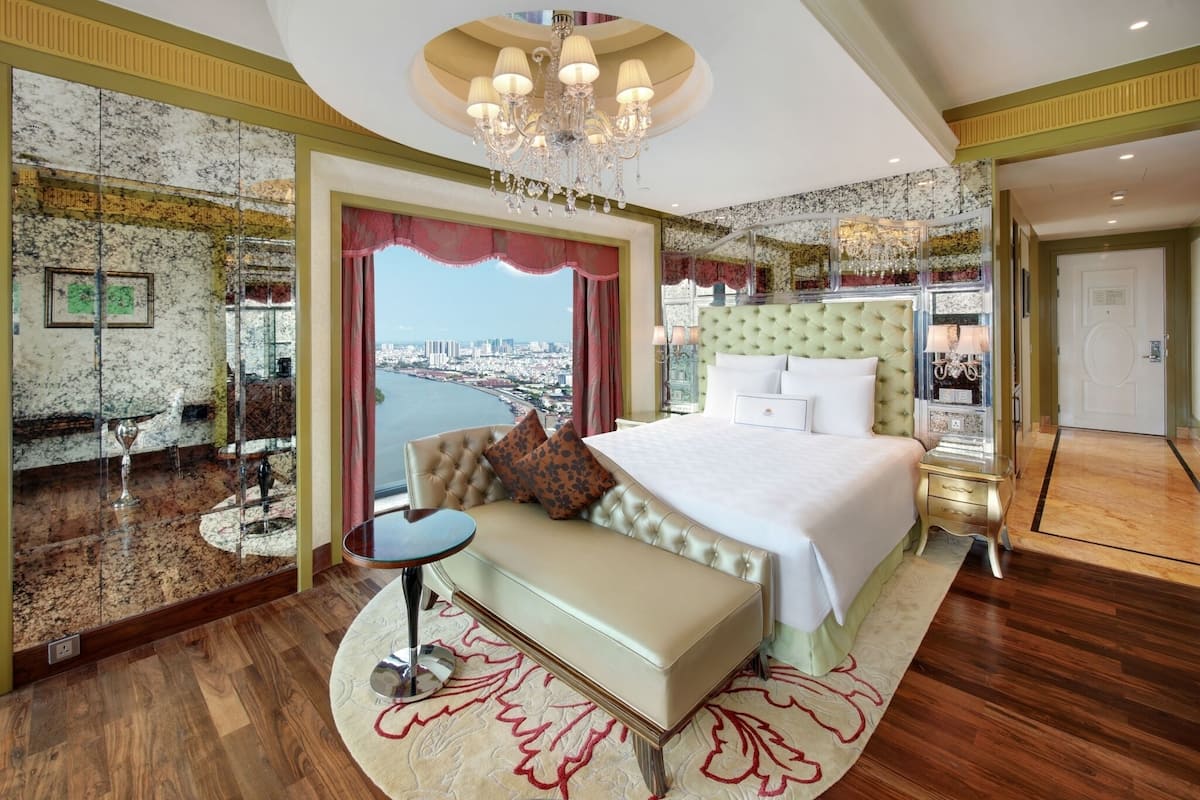 Un dormitorio amplio con una cama grande, un área de descanso, vistas a la ciudad y un candelabro.