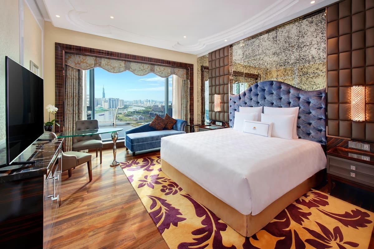 Amplia habitación de hotel con una cama grande, televisión, sofá y vistas al horizonte de la ciudad.