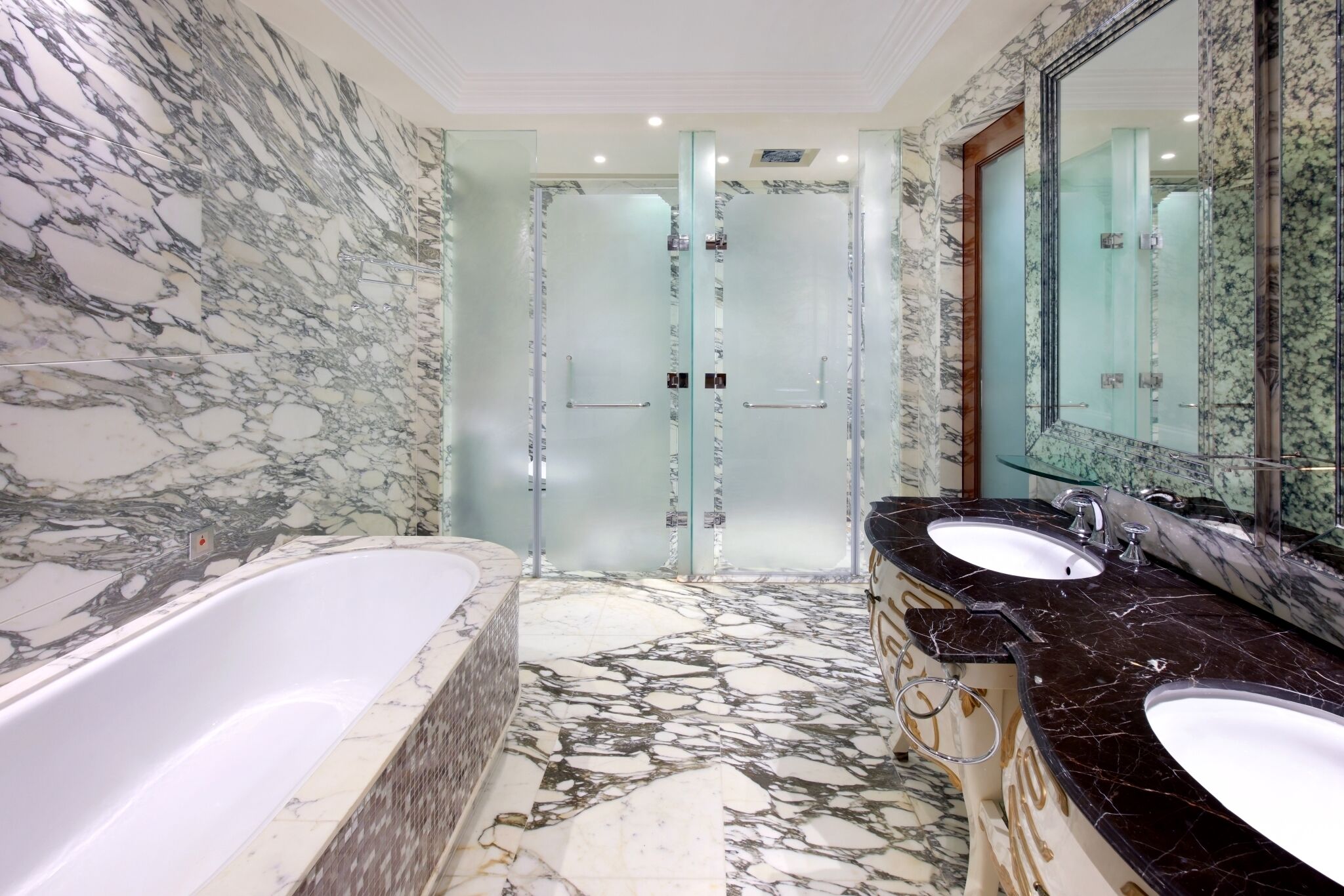 A bathroom with a marble floor, two sinks, a bathtub, and a glass-enclosed shower.