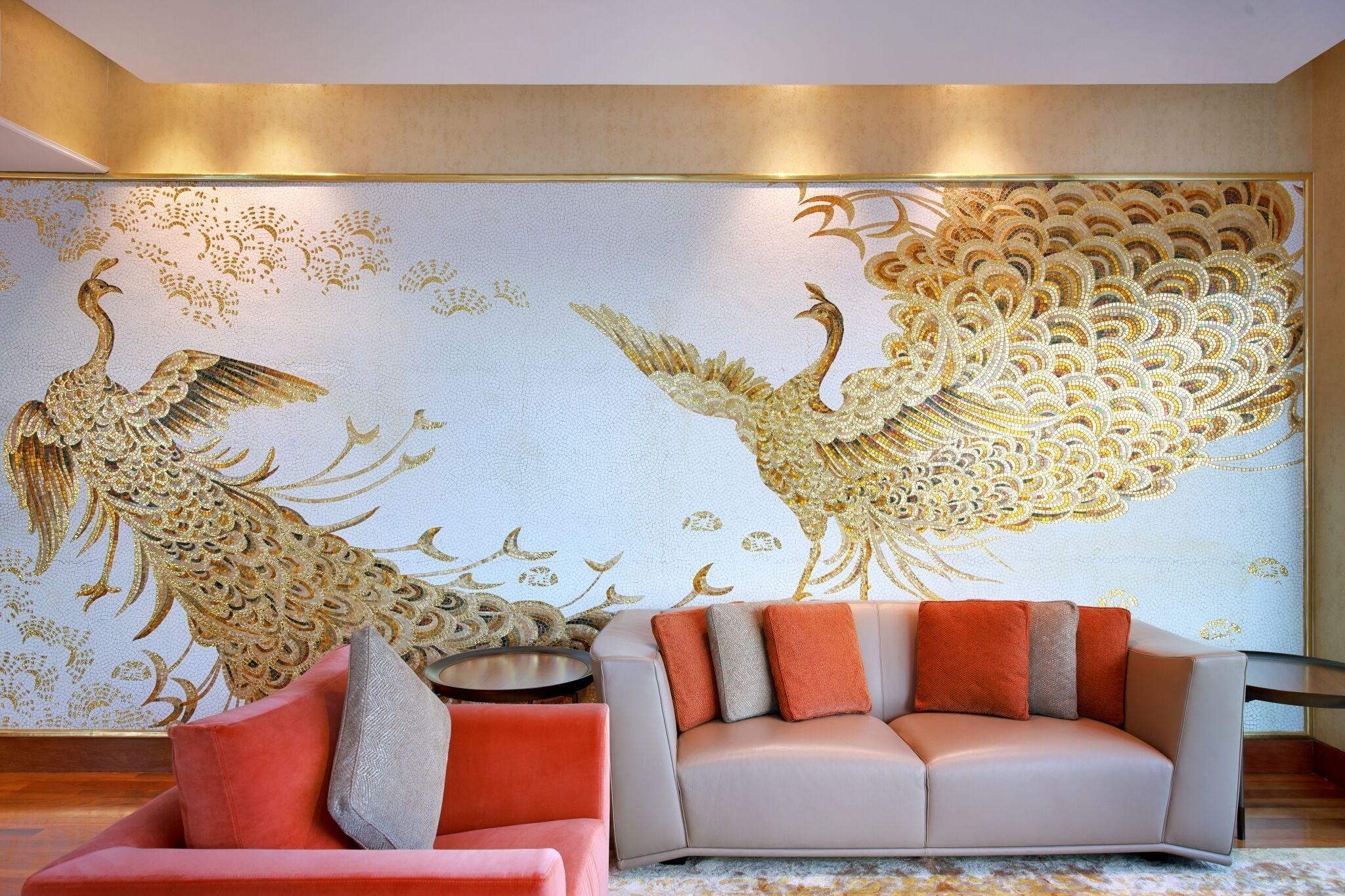 A modern living room with a large wall mural of peacocks, a beige sofa, and a pink armchair.