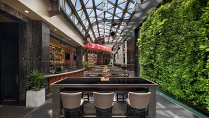 Eine Bar mit einer zentralen Insellounge und Sitzgelegenheiten, umgeben von einer Glaskuppel und einer grünen Wand.