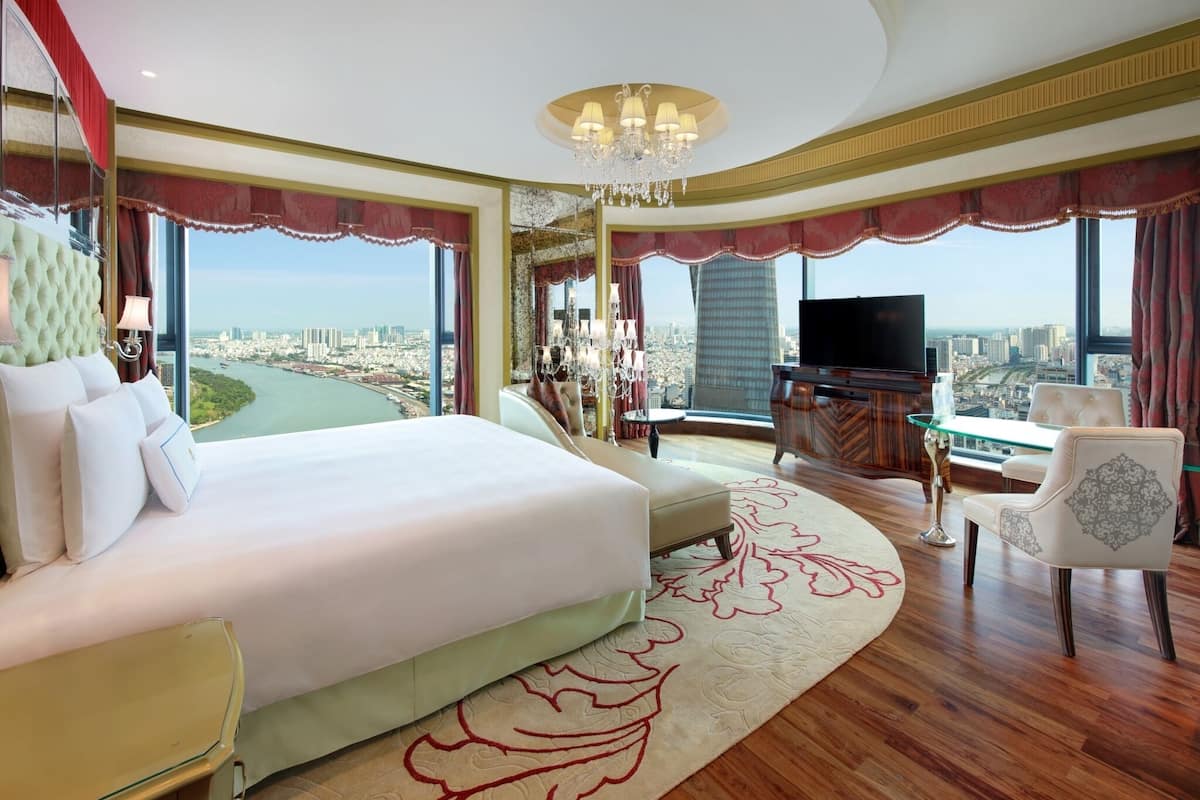 Amplia habitación de hotel con una cama grande, televisión, mesa de vidrio y vista a un paisaje urbano.