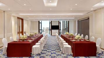 Un salón de conferencias con una larga mesa, sillas blancas y alfombra azul.