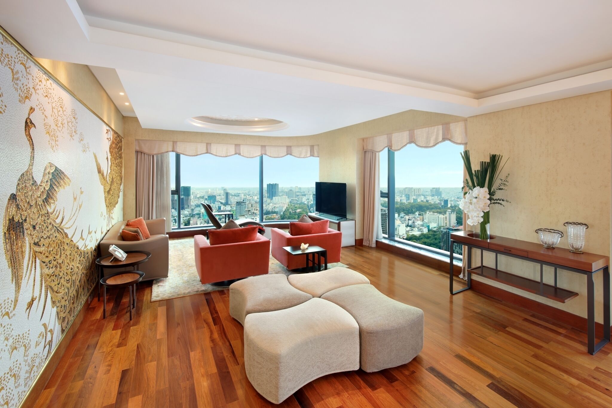 A spacious living room with a large sectional sofa, a flat-screen TV, and a city view through large windows.