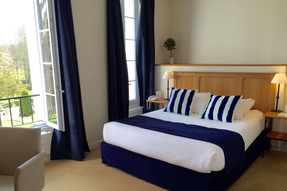 Een hotelkamer met een groot bed, een bureau, een stoel, een raam met gordijnen en een kleine potplant.
