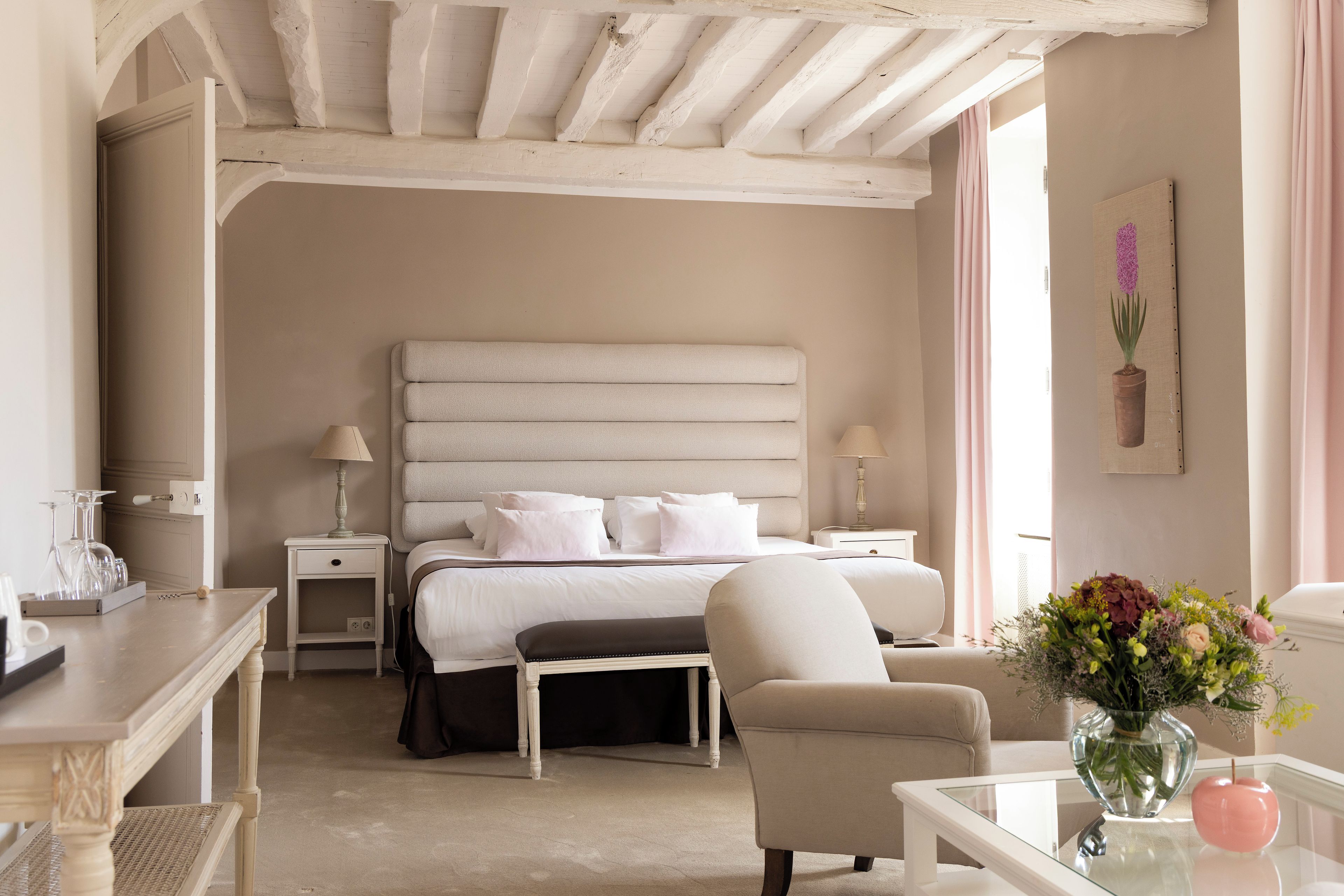 A hotel room with a large bed, bedside tables, a chair, a desk, and a vase with flowers.