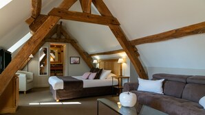 Una camera da letto con soffitto spiovente, un letto, una poltrona e un tavolo.