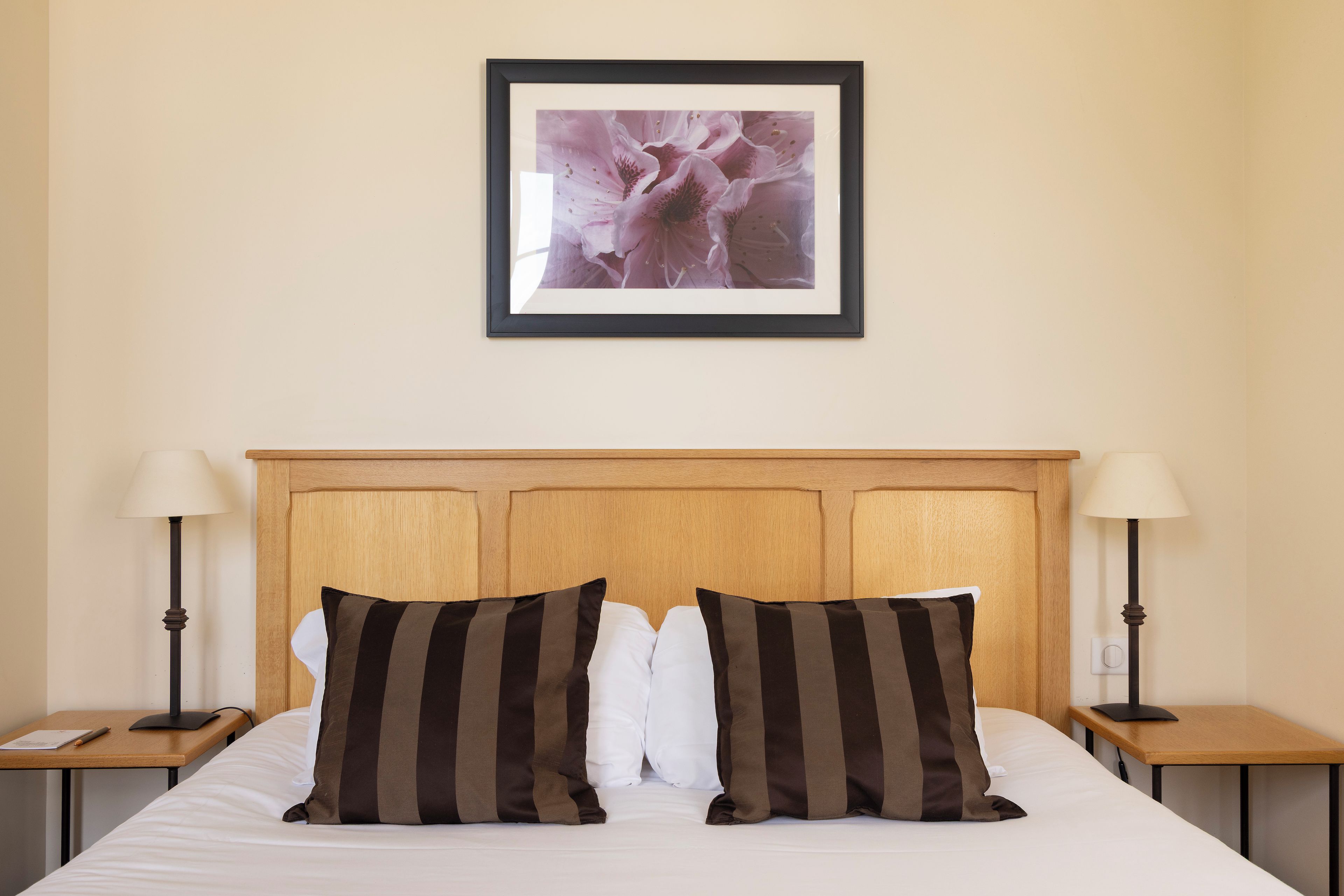 A hotel room with a wooden headboard, two bedside tables with lamps, a bed with white bedding and striped pillows, and a framed picture on the wall.
