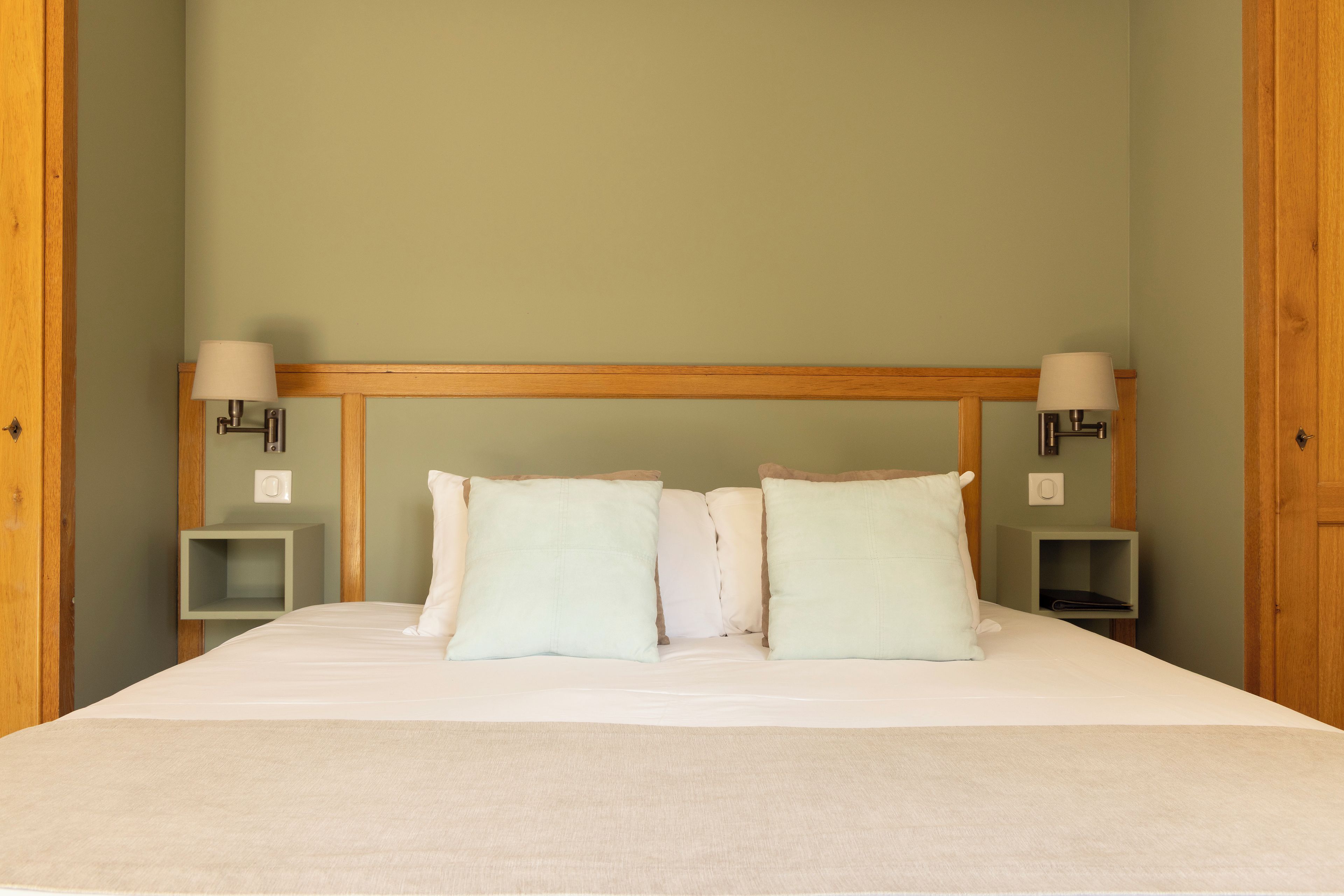 A hotel room with a large bed, two bedside tables, and two wall-mounted lamps.