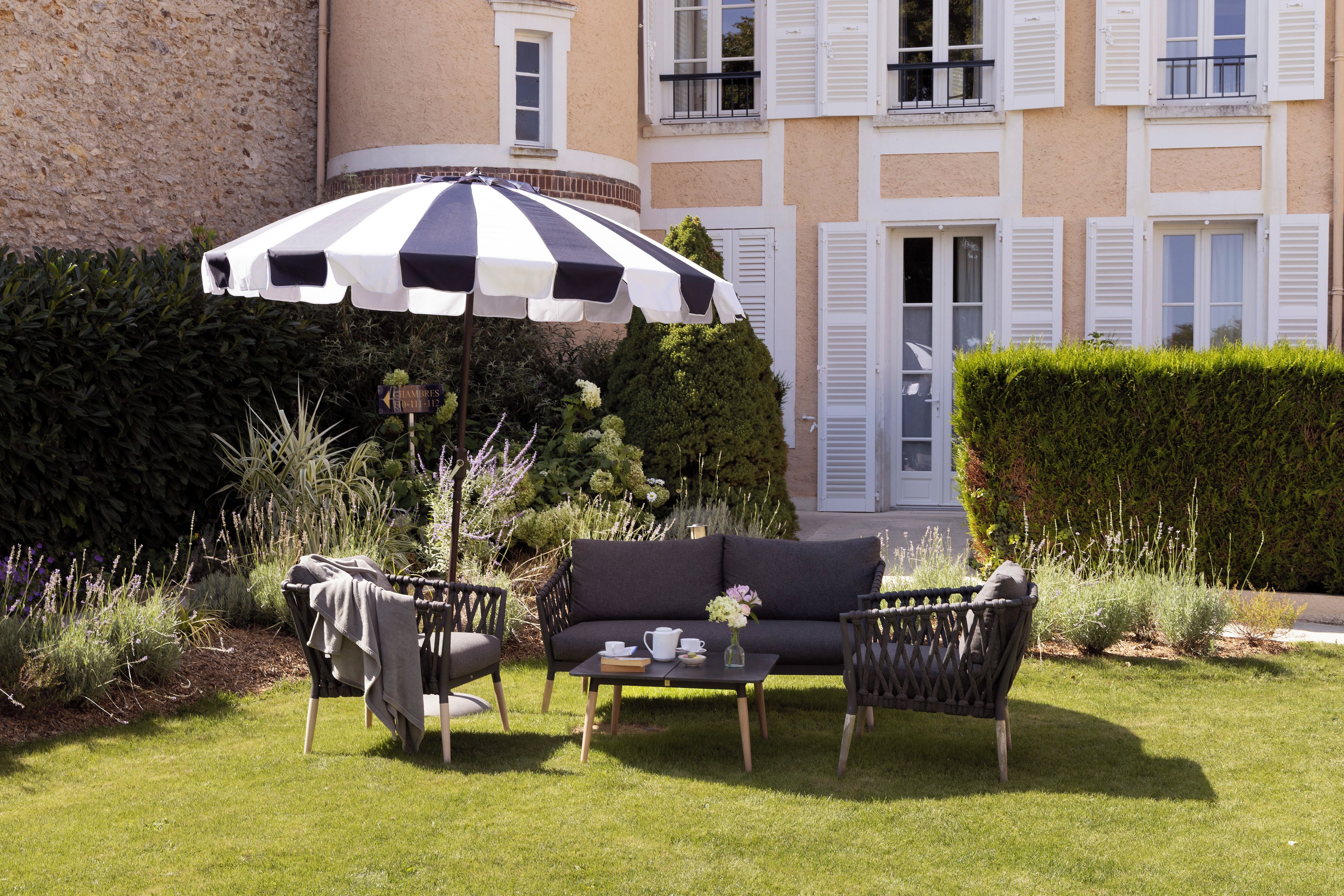 A garden with a black and white striped umbrella, a sofa, and chairs.