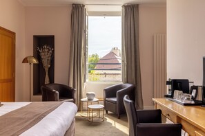 Une chambre d’hôtel comprenant un lit, deux fauteuils, une petite table, un coin café et une vue sur les bâtiments environnants.