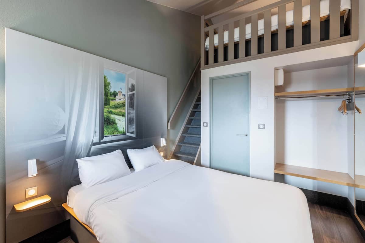 A modern hotel room with a large bed, a nightstand, a wardrobe, and a staircase leading to an upper level.