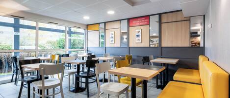 Interior moderno de una cafetería con mesas y sillas, amplias ventanas y vistas a zonas verdes.