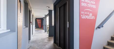 A hallway with a red sign on the wall, a staircase, and a door with a number sign.