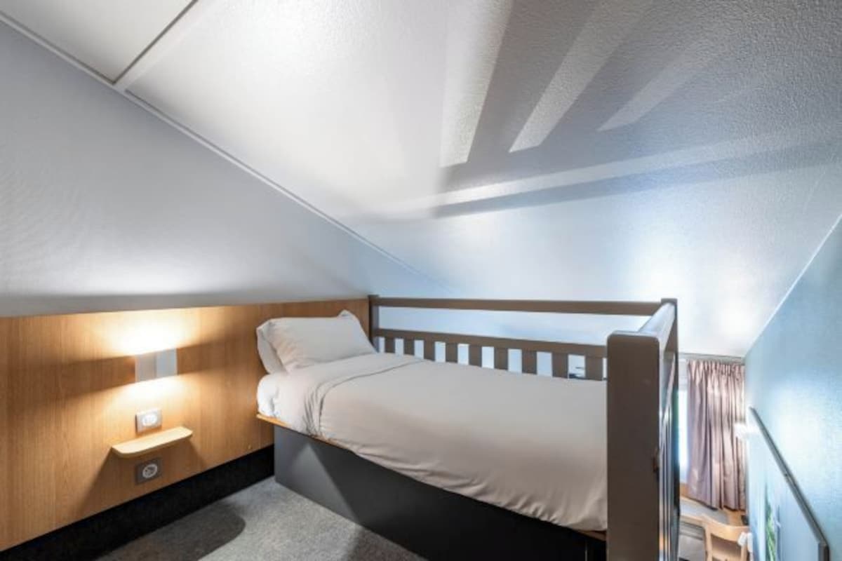 Une pièce compacte et bien éclairée, équipée d’un lit superposé, d’une table de chevet et d’un luminaire fixé au mur.