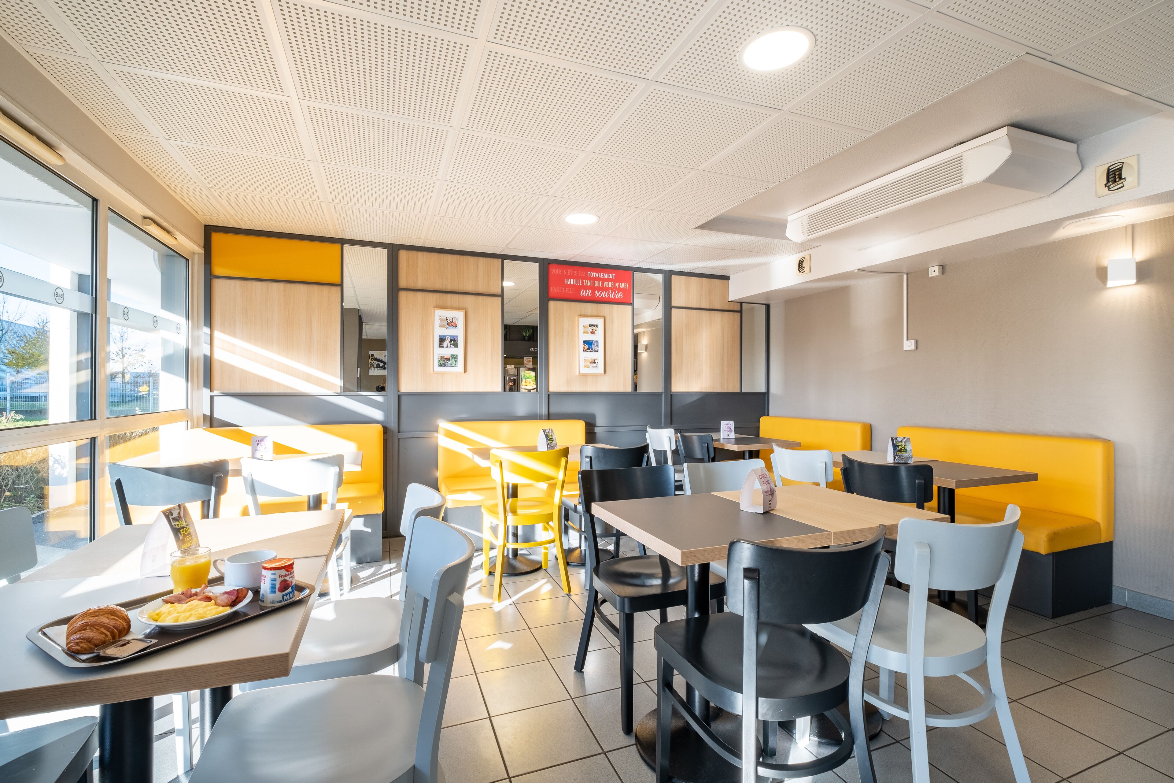 A modern dining area with tables and chairs, a menu board, and a view of the outside.