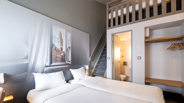 Una habitación de hotel moderna con una cama grande, una escalera, un armario y un cuadro con una vista urbana enmarcada.