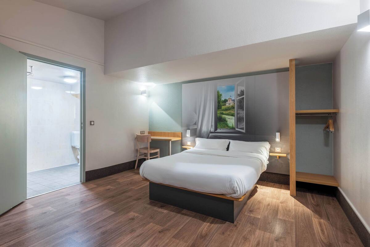 A modern bedroom with a large bed, bedside tables, a desk, and a view of a garden through a window.