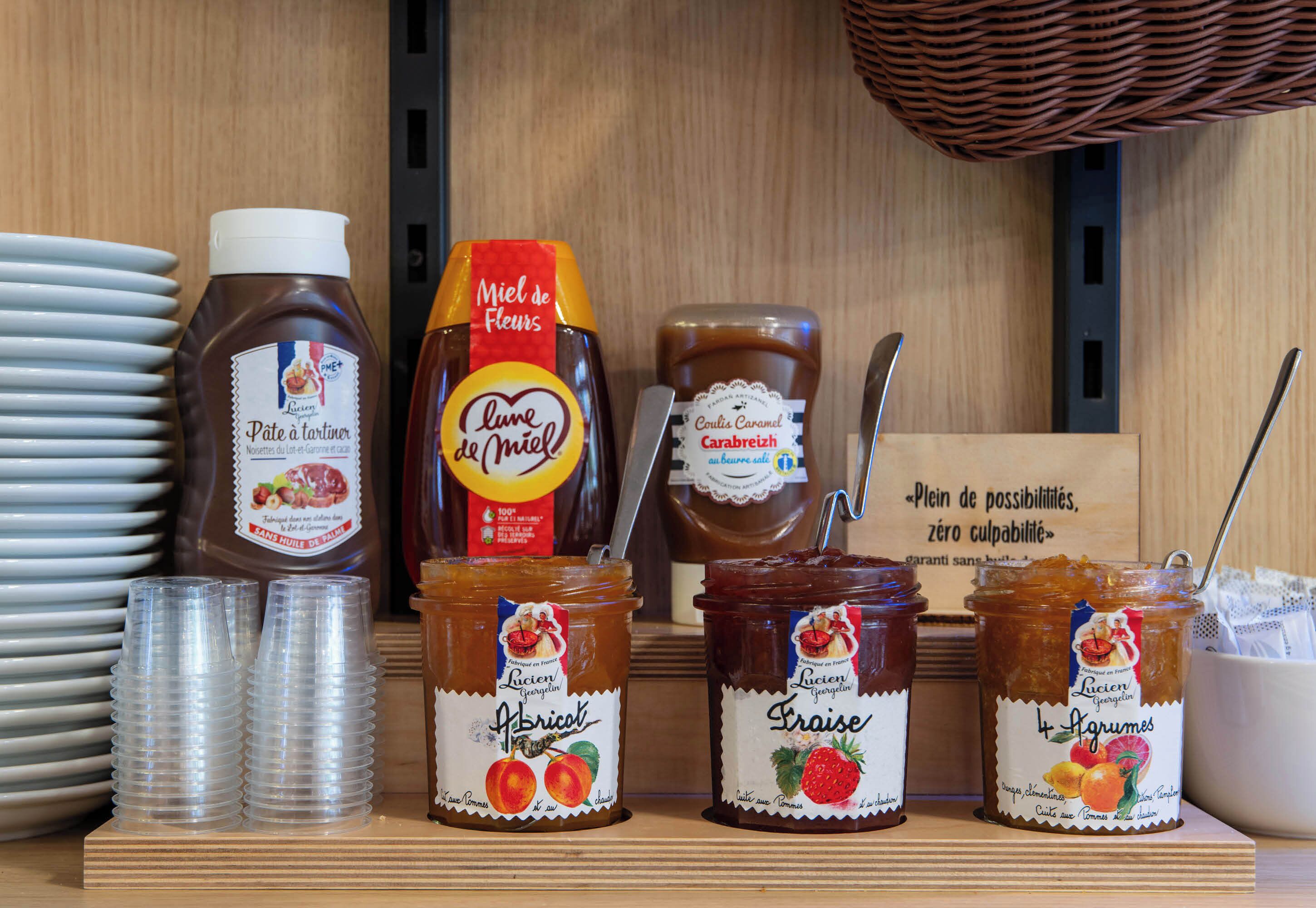 A display of various jars of preserves and sauces, including apricot and strawberry, on a wooden shelf.